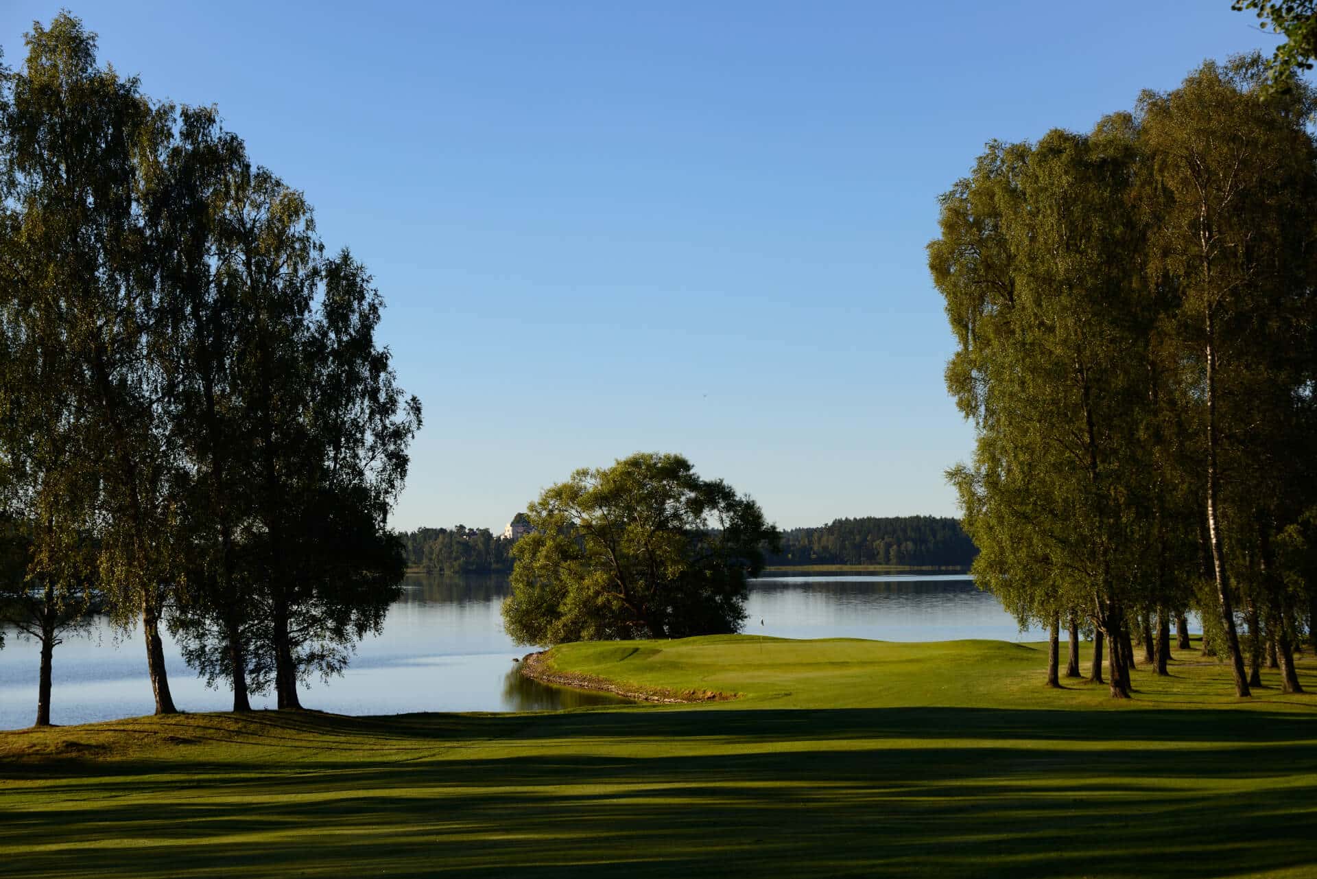 Täby Gold Klubb golf course view over fairway and over lake with trees and bright blue sky